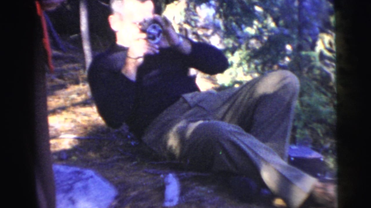 Man seated on a forest floor holding a camera to his eye.