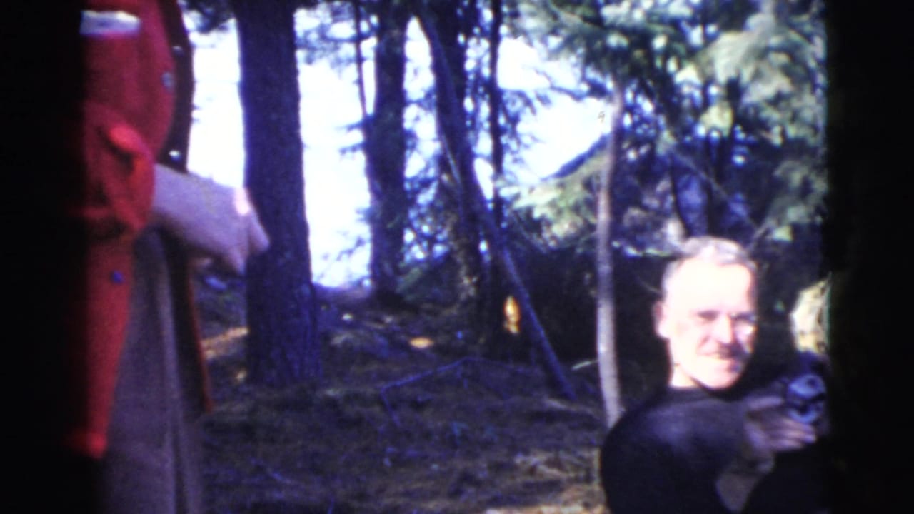 Woman in a red jacket standing among trees near a seated man.