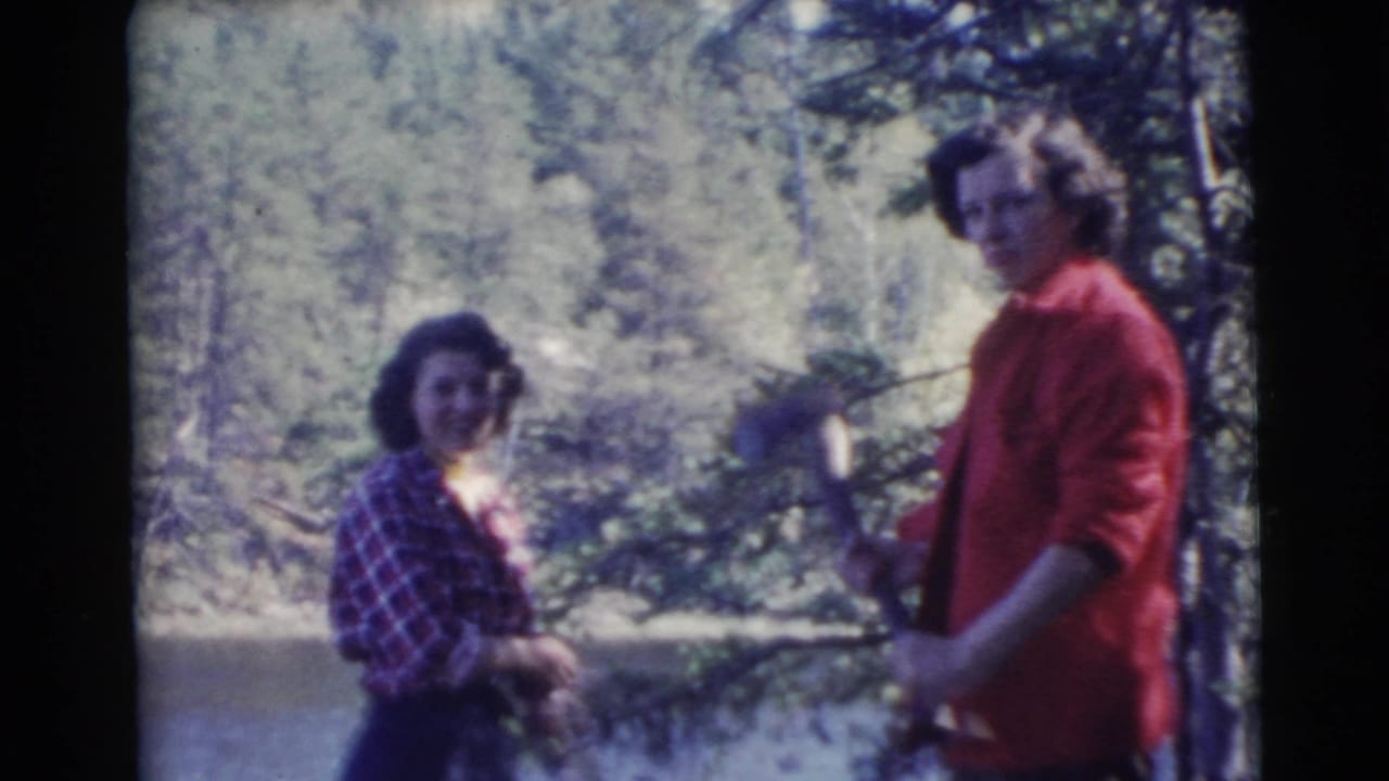 Two adult women in a wooded Miami riverside setting, with one in a red shirt holding a long branch or axe handle while the other smiles nearby.