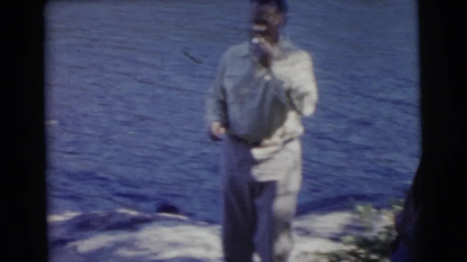 The man stands at the Miami lakefront with his hand near his mouth, likely smoking, while water fills the background.