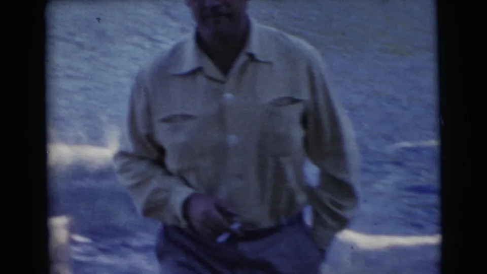 1956 Miami frame with an adult man in a light shirt and trousers standing by the river in blue-shifted 8mm color.