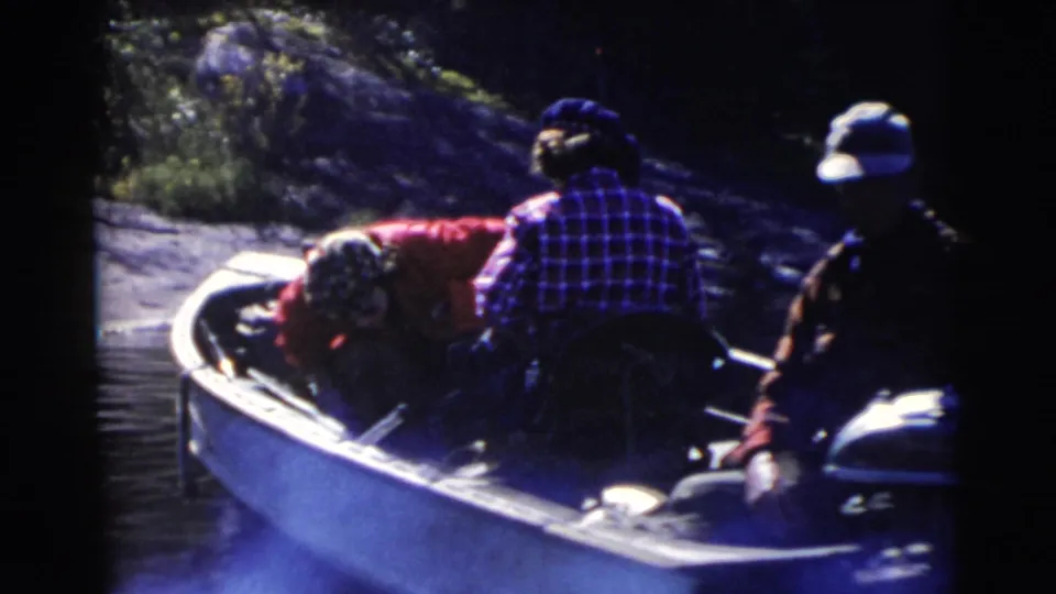 1956 Miami home-movie frame of adults riding in a small canoe on calm water near trees and shoreline.