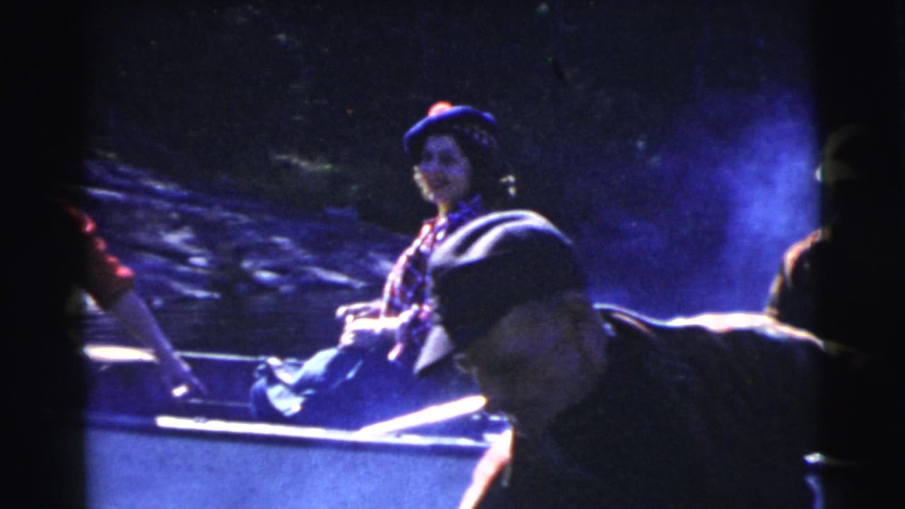 A woman in a patterned hat sits in a rowboat while a man in a cap leans in the foreground.