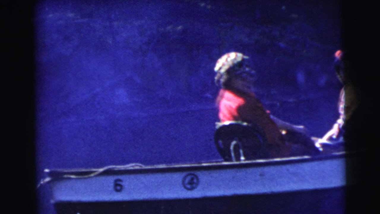 1956 Miami home-movie frame with a red-clad passenger seated in a small motorboat, its side number partly visible in blue shadow.