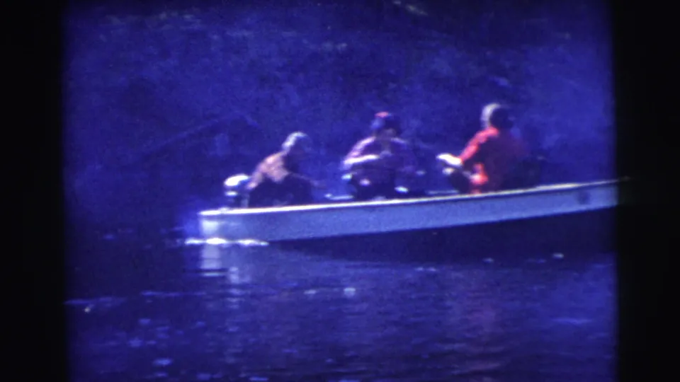 Wide 1956 Miami home-movie frame showing a small boat crossing dark water with several seated passengers under a strong blue cast.