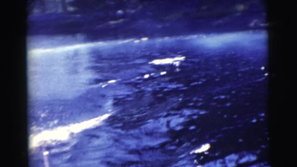 1956 Miami home-movie frame showing the boat's bright wake trailing across dark blue water near shore.