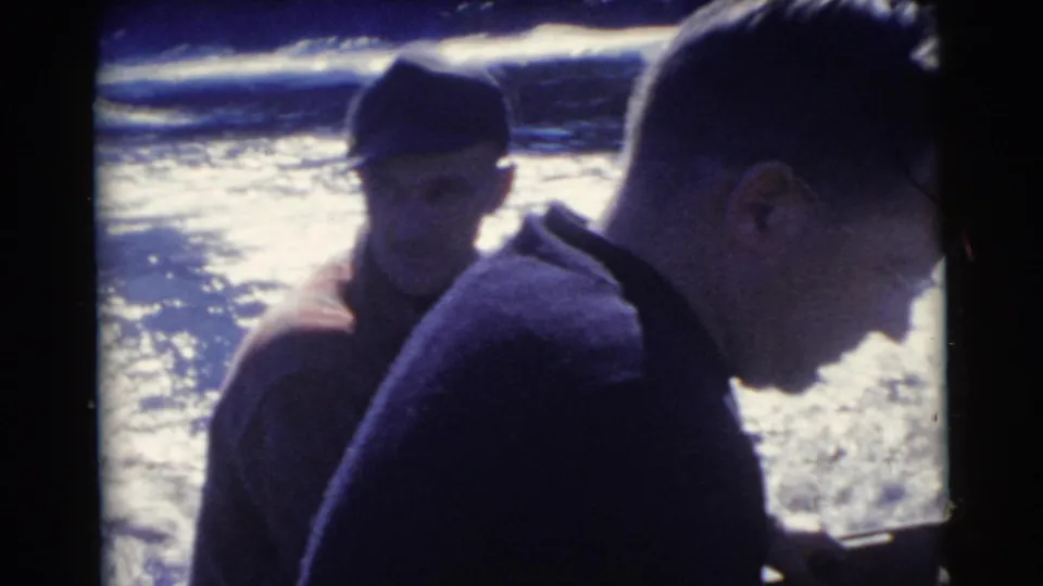 1956 Miami 8mm frame showing two adult men on a boat, filmed close up against bright reflective water.