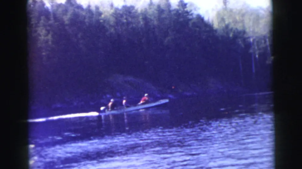 A small boat carrying people passes through a shaded, wooded water scene in archival 8mm footage from Miami, 1956.