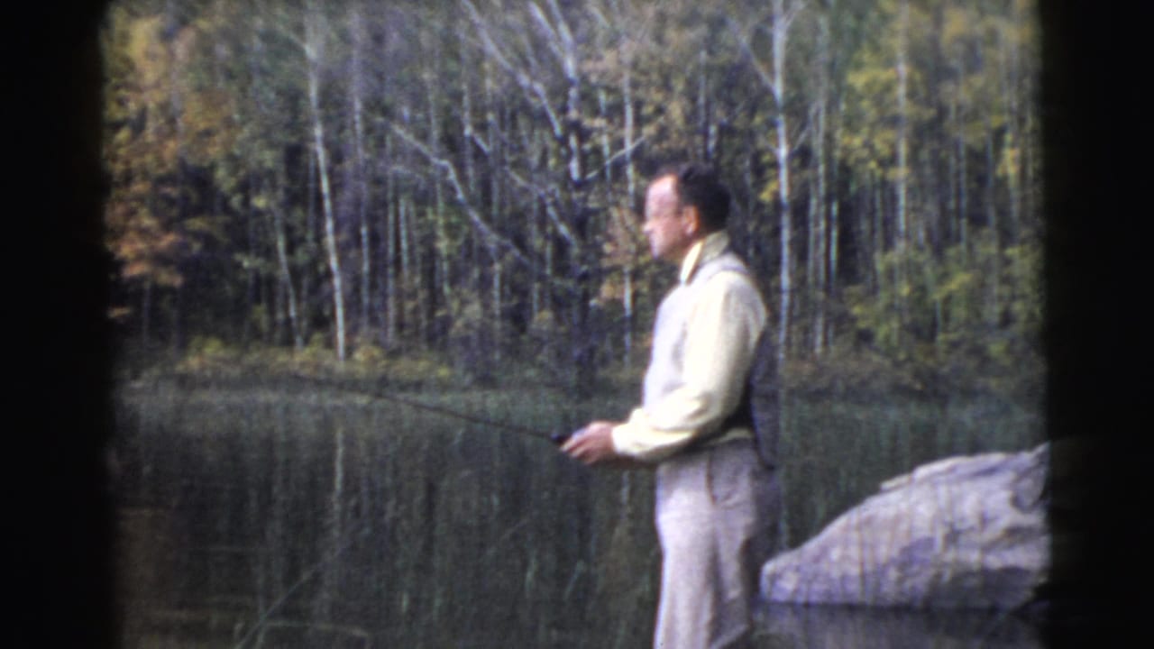Man stands in profile by a lake holding a fishing rod.