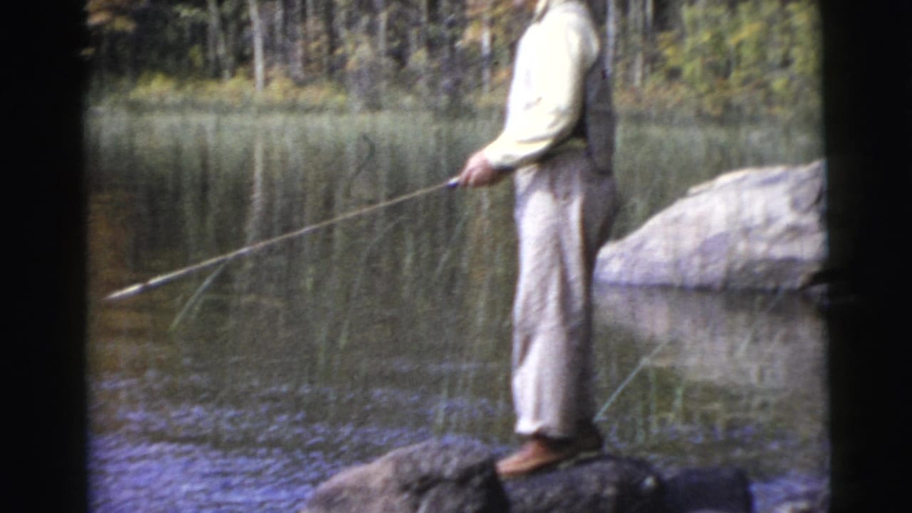 Man stands on a shoreline rock while extending a fishing rod over the water.