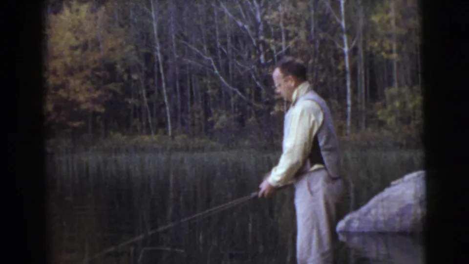 The man remains in profile beside the Miami lake, holding his rod low over the water with trees reflected behind him.