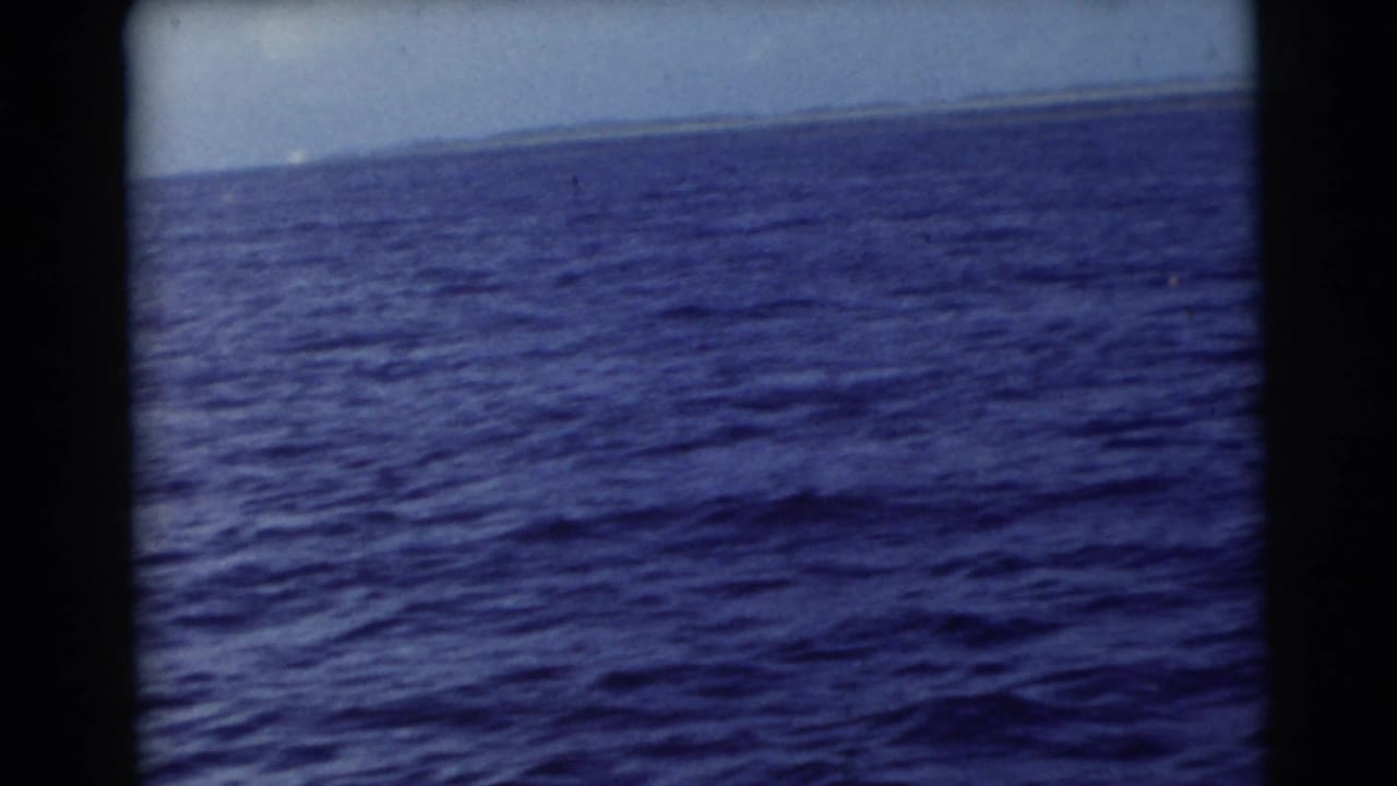 Open blue water with a distant horizon, framed by dark film borders.