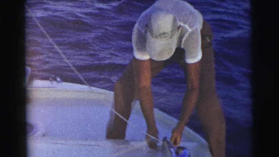 A 1956 Miami 8mm frame shows the man bent over near the boat edge, tying or adjusting a rope above the water.