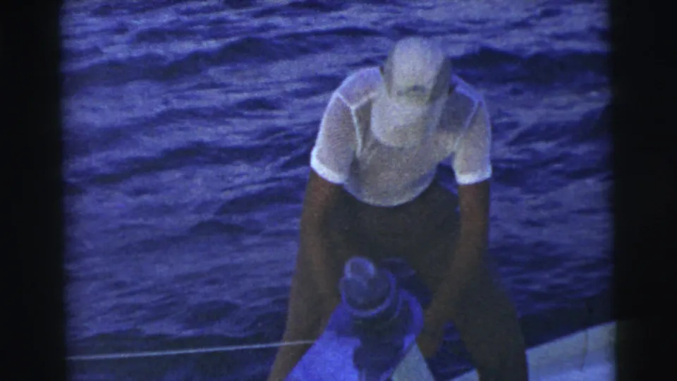 A man bends over a line near a cleat or deck fitting as the small boat sits against choppy blue water.