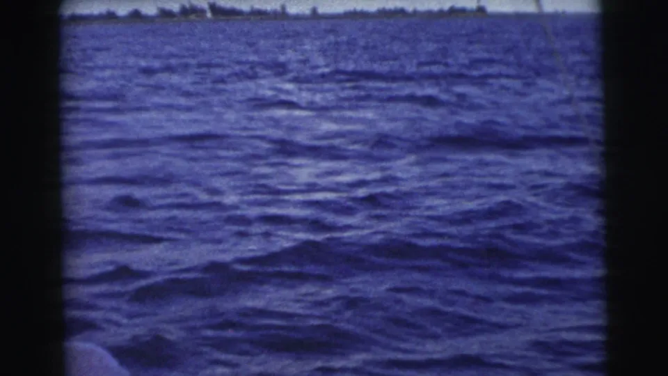 1956 Miami home-movie frame looking over rippled blue water toward a low, distant shoreline under bright daylight.