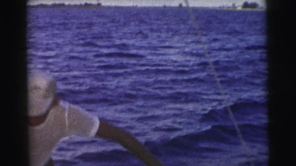 1956 Miami frame showing a person near the boat side, with a thin fishing line visible over dark blue ocean water.