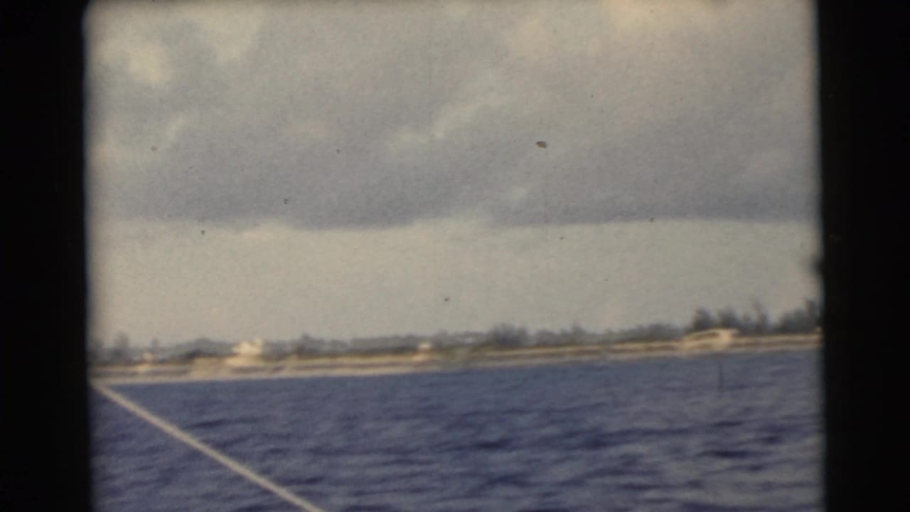 Boat-level view across water toward a low shoreline beneath a gray cloud bank.