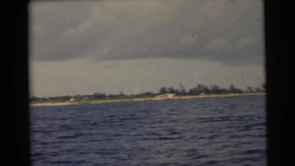 1956 Miami-area 8mm frame showing a distant coastal strip, tree line, and choppy water from a moving boat.