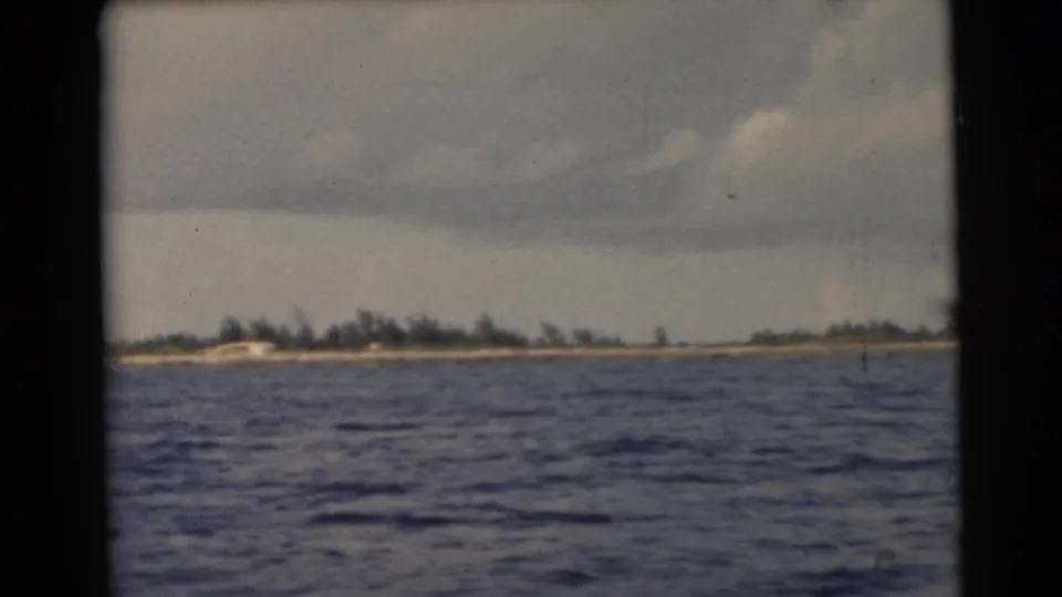 1956 Miami-area home-movie view from a boat, showing open water, a flat coastal horizon, trees, and muted cloudy light.
