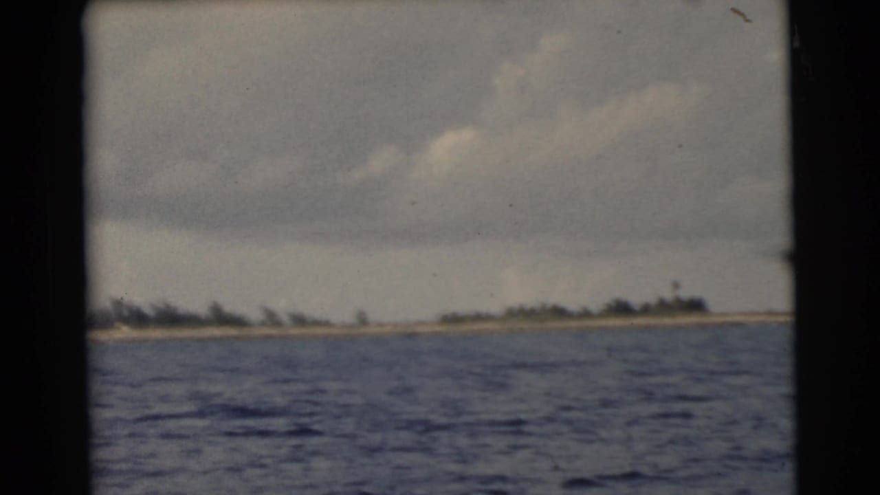 Blue water with a distant sandy shoreline and trees under a cloudy sky.