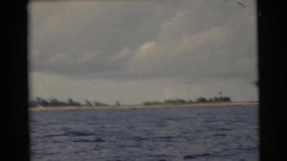 1956 Miami-area 8mm frame showing open blue water and a low tree-lined shoreline beneath clouds.