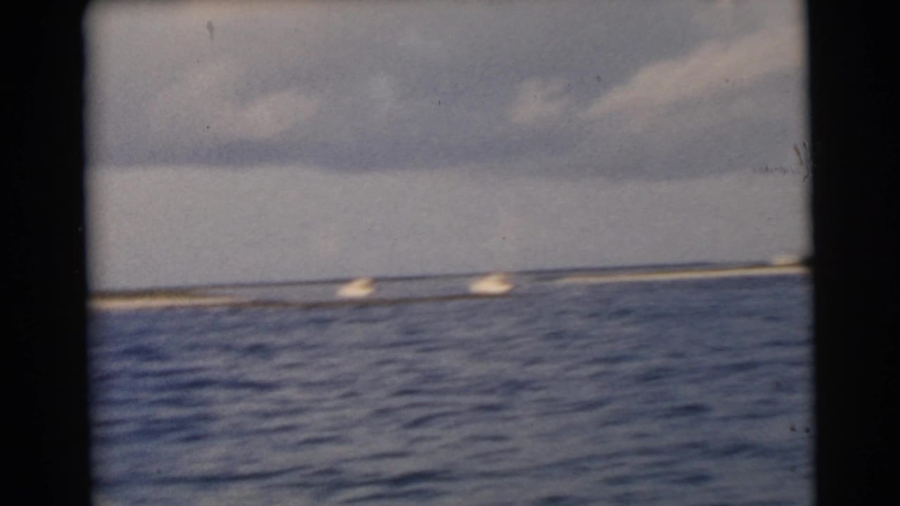 Small boats travel across blue water near a distant low shoreline under clouds.
