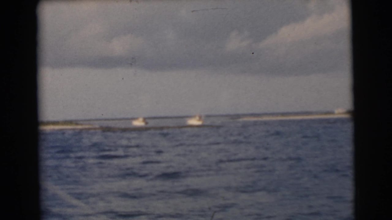 Two small boats pass near a low strip of shoreline across rippled water.