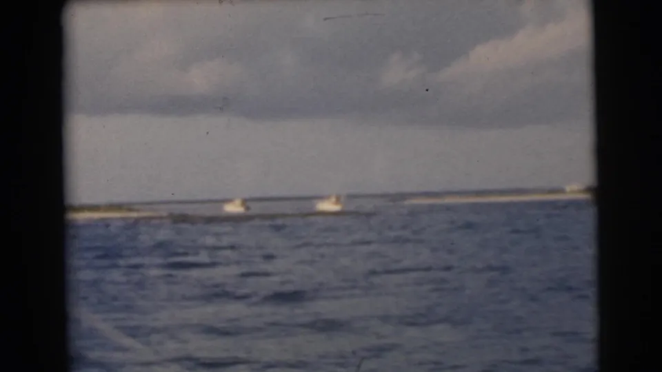 Small white boats move near a distant Miami shoreline in soft, grainy 1950s 8mm color footage.