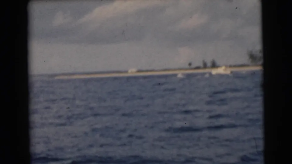 Open blue water and distant boats appear near a low Miami shoreline, with soft 8mm color and visible frame edges.