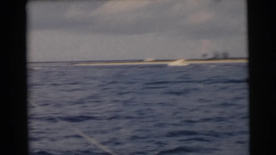 1956 Miami-area coastal frame with rippled water in the foreground and a low shoreline stretching across the horizon.