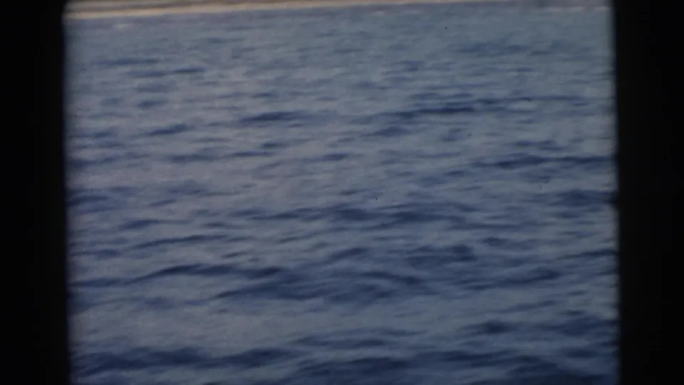 A soft 8mm frame dominated by rippled blue water, likely filmed from a moving boat in the Miami area in 1956.
