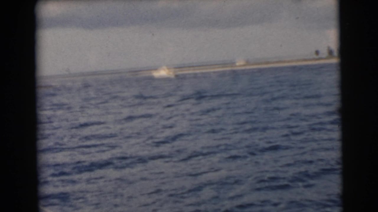 Blue water seen through dark boat-window borders with a distant shoreline under cloudy sky.