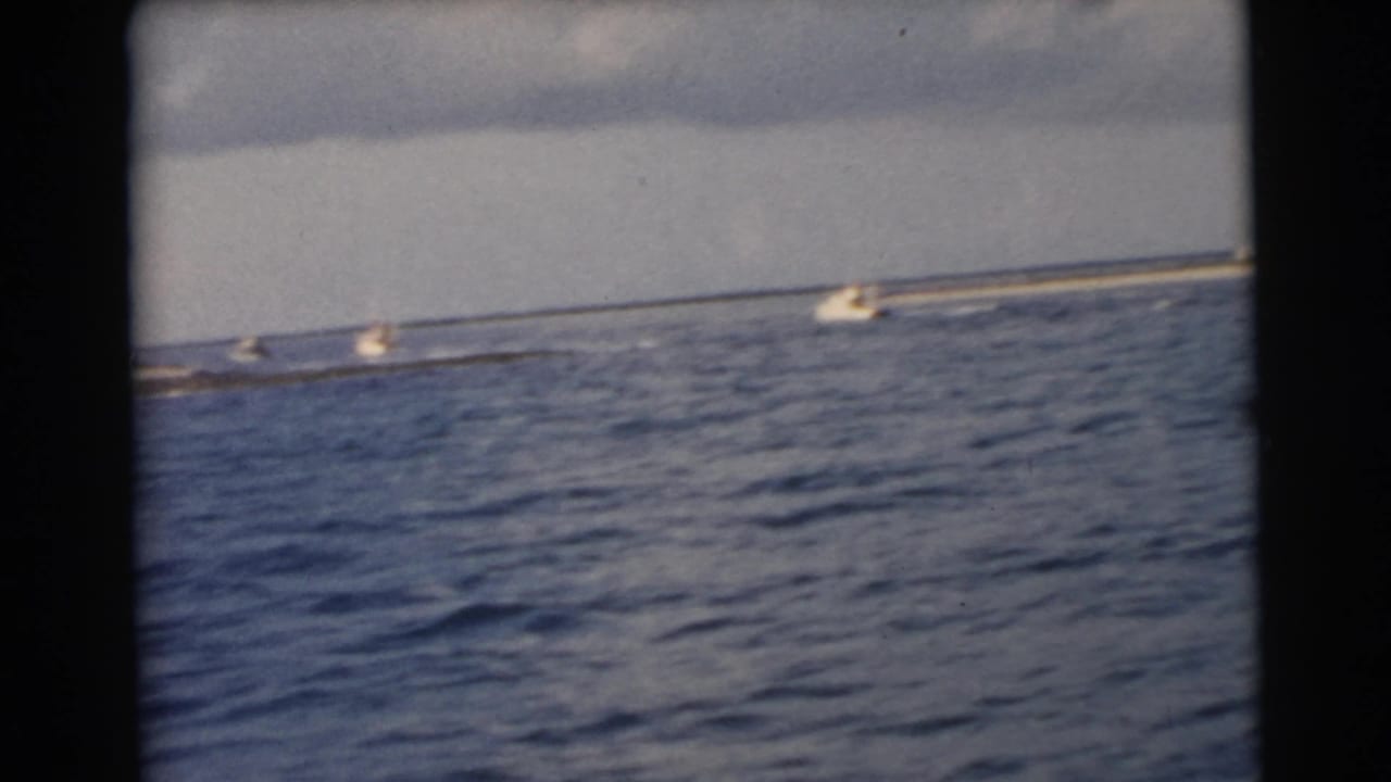 Distant small boats on blue water with a low shoreline beyond them.