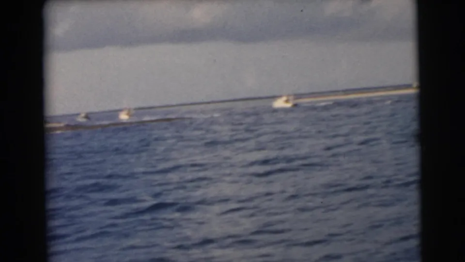 1956 Miami-area 8mm frame of small boats moving near a distant shoreline, viewed from inside a boat over choppy water.