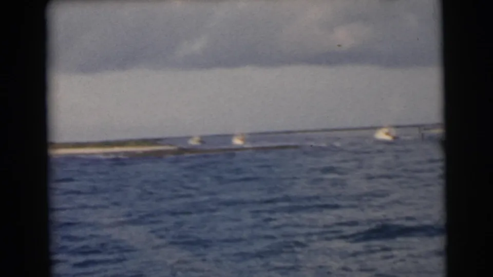 1956 Miami-area 8mm frame with choppy foreground water and small boats near a low beach or shoreline in the distance.
