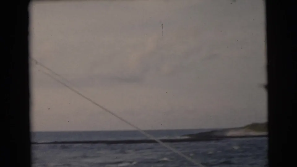 1956 Miami-area 8mm frame showing open water and cloudy sky from a boat, with a low shoreline or landform at the right.