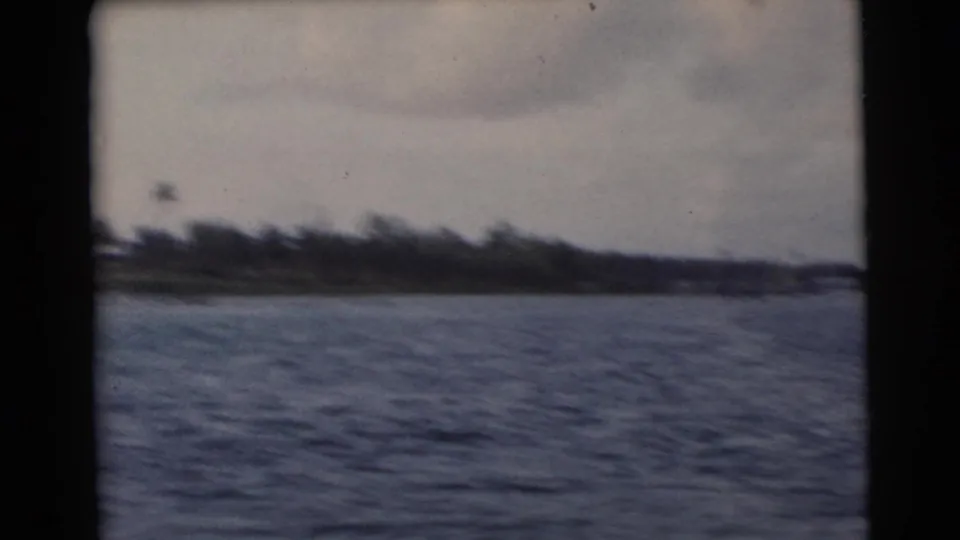 Soft 8mm frame of a low Miami-area coast passing in the distance beyond choppy water.