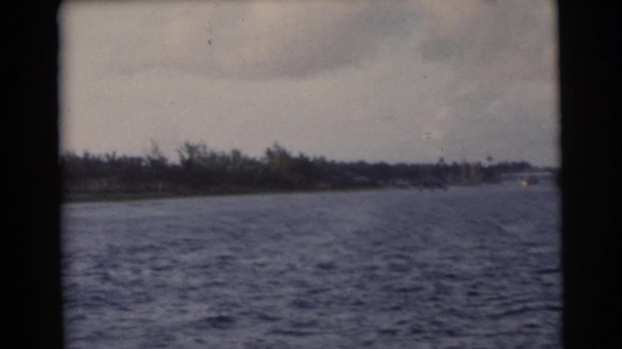 1956 Miami-area home-movie view across choppy water toward a low tree-lined shore under clouds.