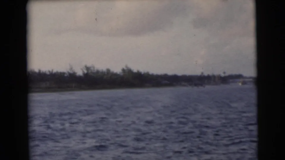 1956 Miami-area home-movie view across choppy water toward a low tree-lined shore under clouds.