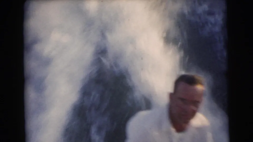 At the end of the 1956 Miami boating clip, a seated man is partly cropped at frame right while a large burst of water spray fills the background.