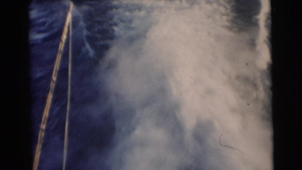 1956 Miami 8mm home-movie frame showing deep blue water, foamy wake, and a diagonal tow rope during water-skiing action.