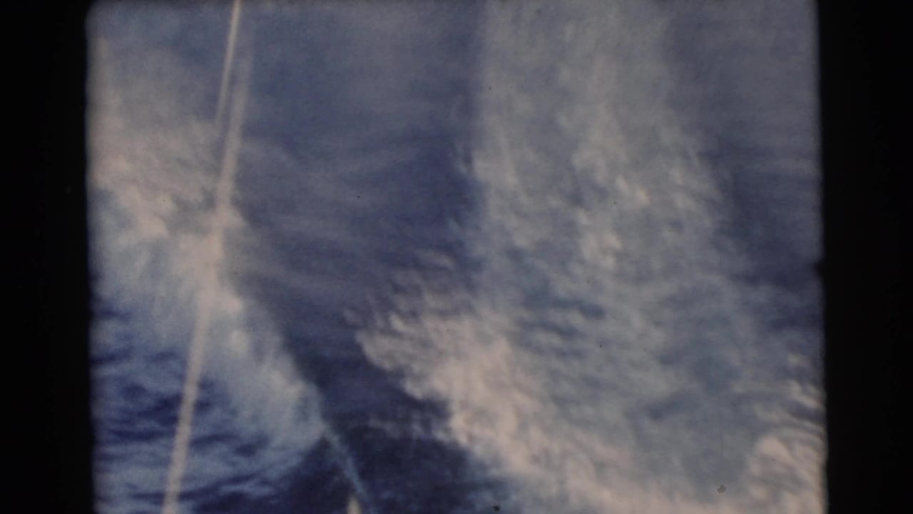 1956 Miami 8mm frame with turbulent white wake and a pale tow line over deep blue ocean water.