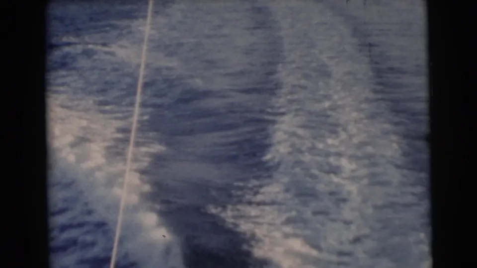 1956 Miami home-movie frame showing rippled blue water, white wake foam, and a tow line near the left side.