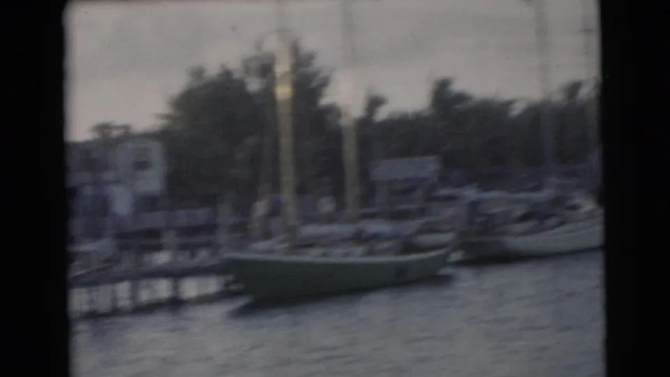 1956 Miami 8mm frame showing sailboats at a dock, choppy water, masts, shoreline buildings, and palms under an overcast sky.