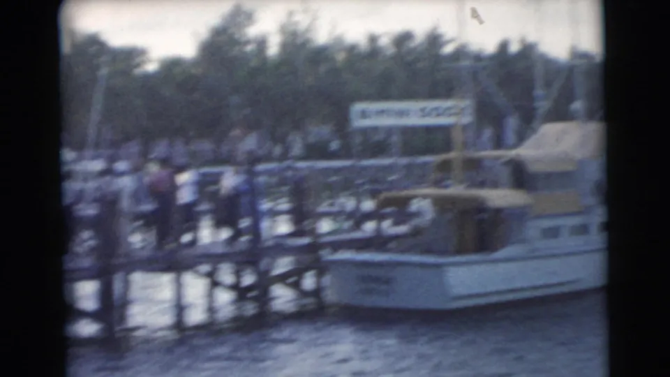 Soft 8mm frame of a 1956 Miami marina, showing people gathered on a pier beside a moored boat and Bimini Dock signage.