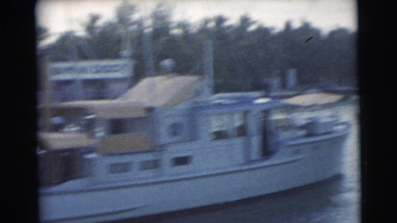 A soft 8mm frame shows the white cabin boat at the Miami dock, with the background trees and dock structures blurred by motion.
