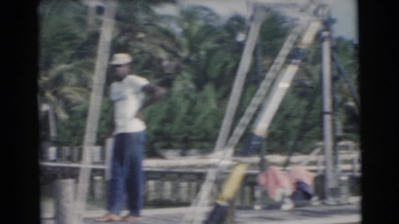 Adult man stands on a wooden dock among palms, railings and fishing gear.