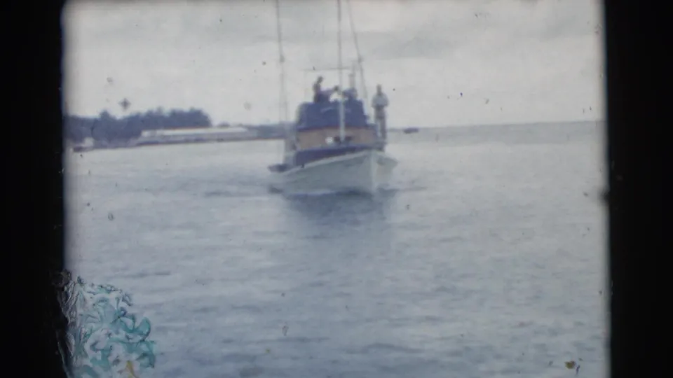 A small boat with several people aboard moves across the water in this 1956 Miami-area waterfront home-movie frame.