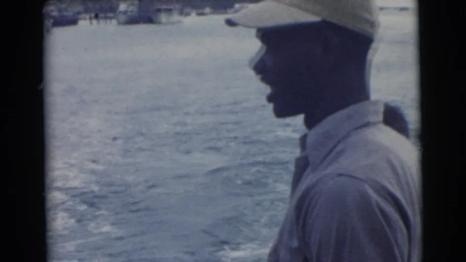 Close dockside profile of a man in a light cap and shirt against open water in 1956 Miami-area 8mm footage.