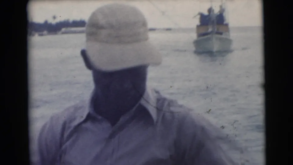 A man in a cap stands aboard a boat in Miami, with open water and a small distant vessel visible behind him.